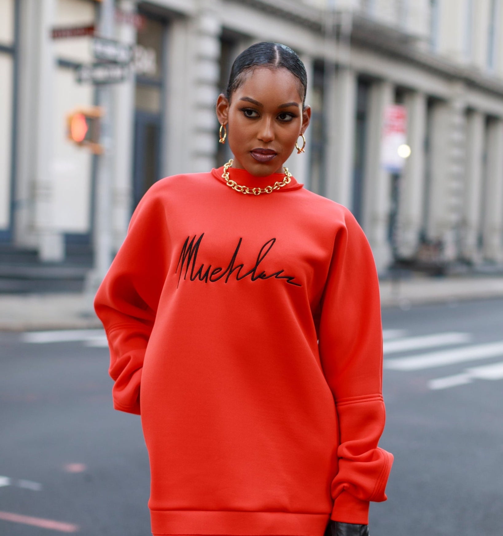 Person wearing a bright red outfit with 'Muehleder' text on a city street.