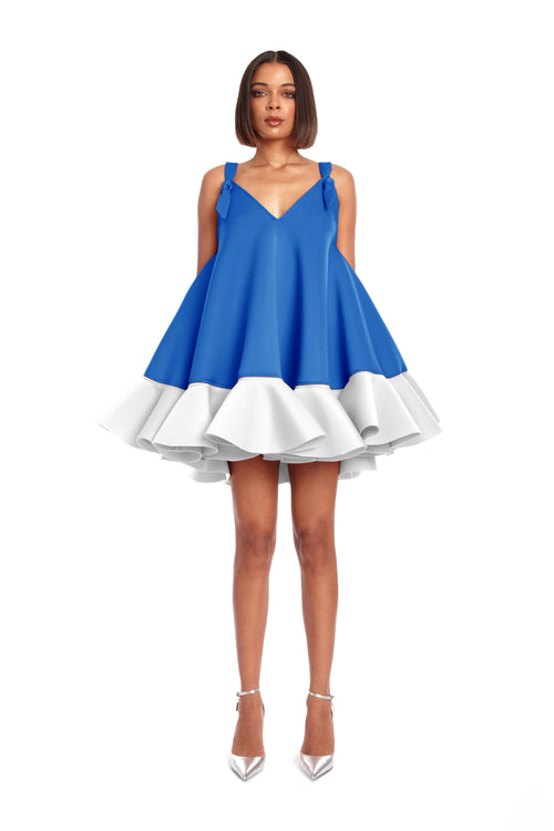 A woman modeling a blue sleeveless mini dress with a v-neckline and white ruffles at the hemline.