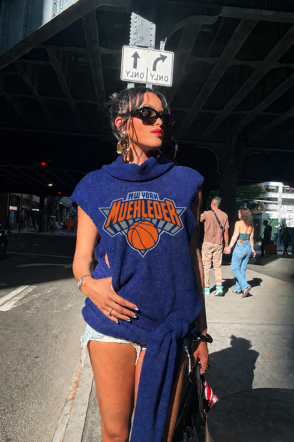 Woman wearing a blue sweatshirt with a logo, standing on a street.