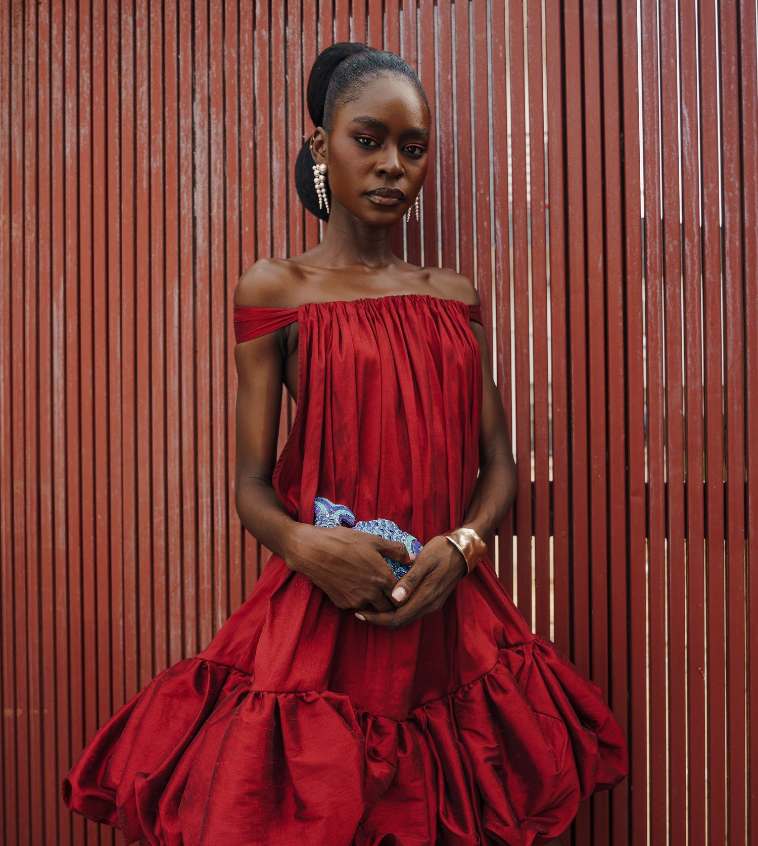 Woman wearing a red off-shoulder dress against a red wooden panel background