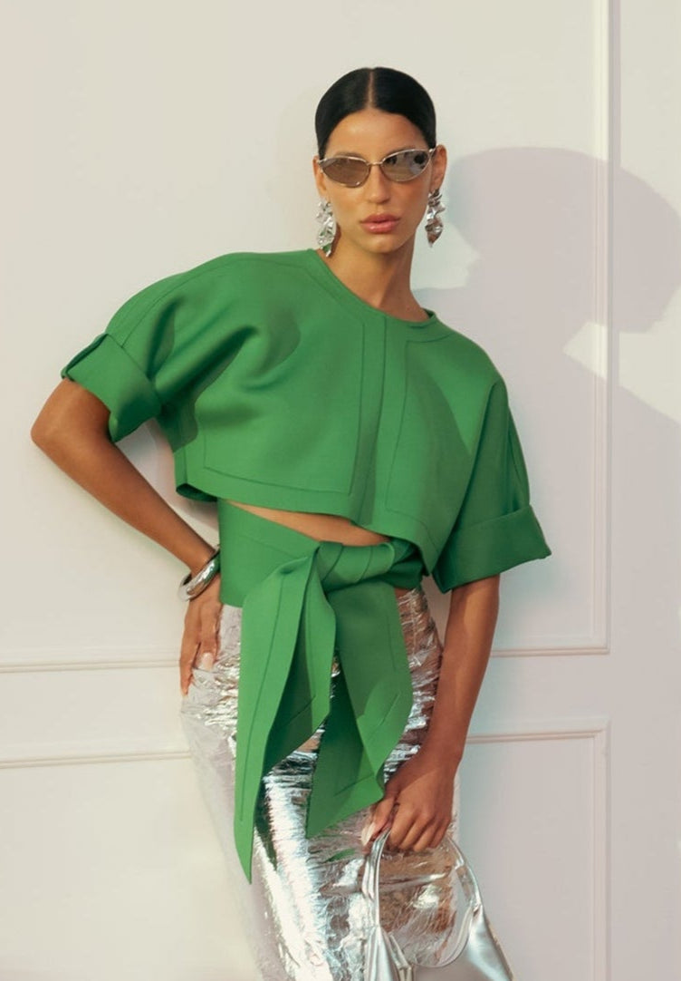 Woman wearing a green top and silver skirt with sunglasses indoors.