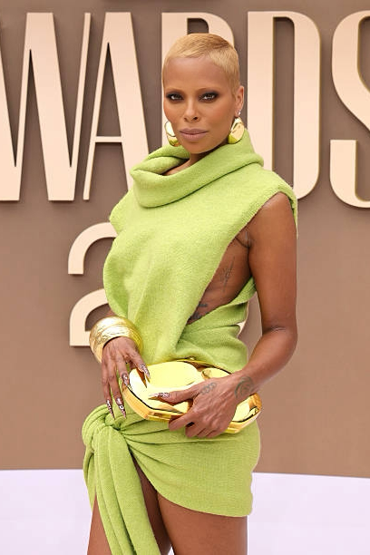 eva marcille wearing a green dress with a high slit, holding a clutch, against an awards ceremony backdrop.