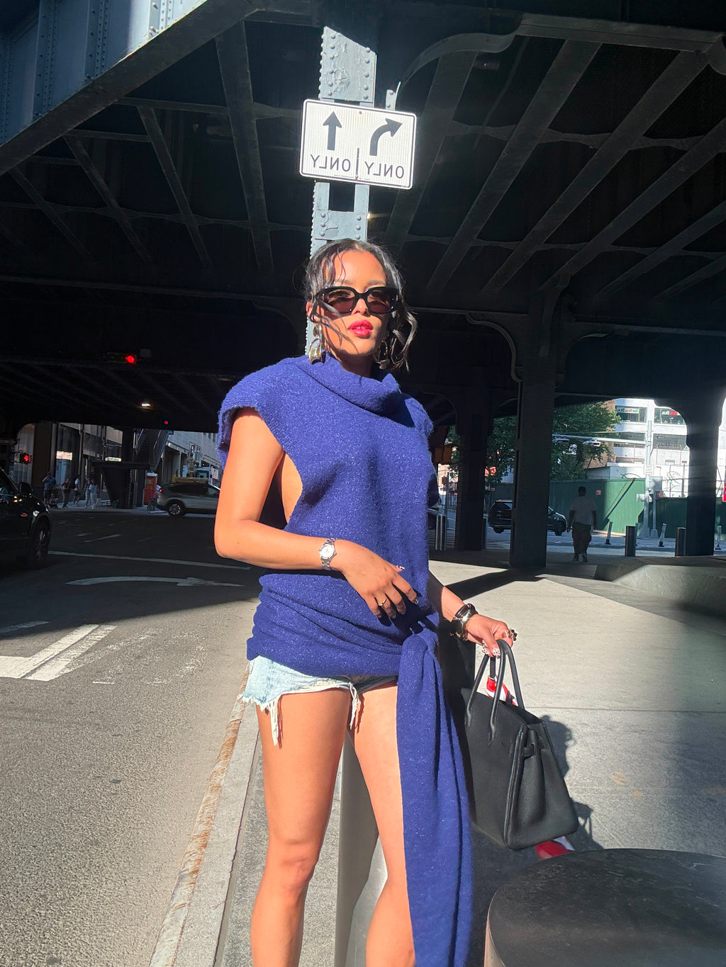 Woman in a blue dress standing on a city street with a black handbag.