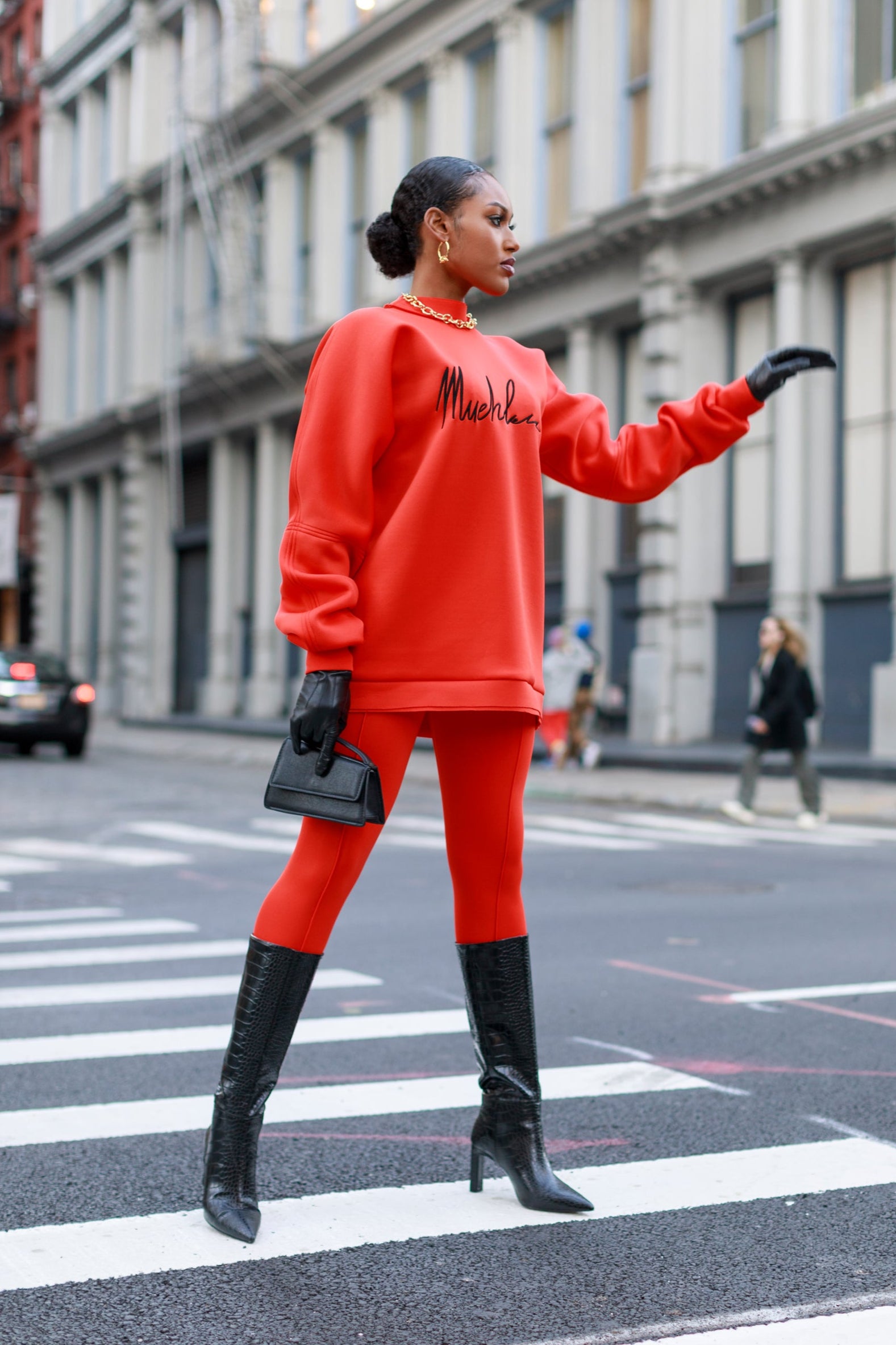 Person wearing a bright red outfit with black boots crossing a city street.