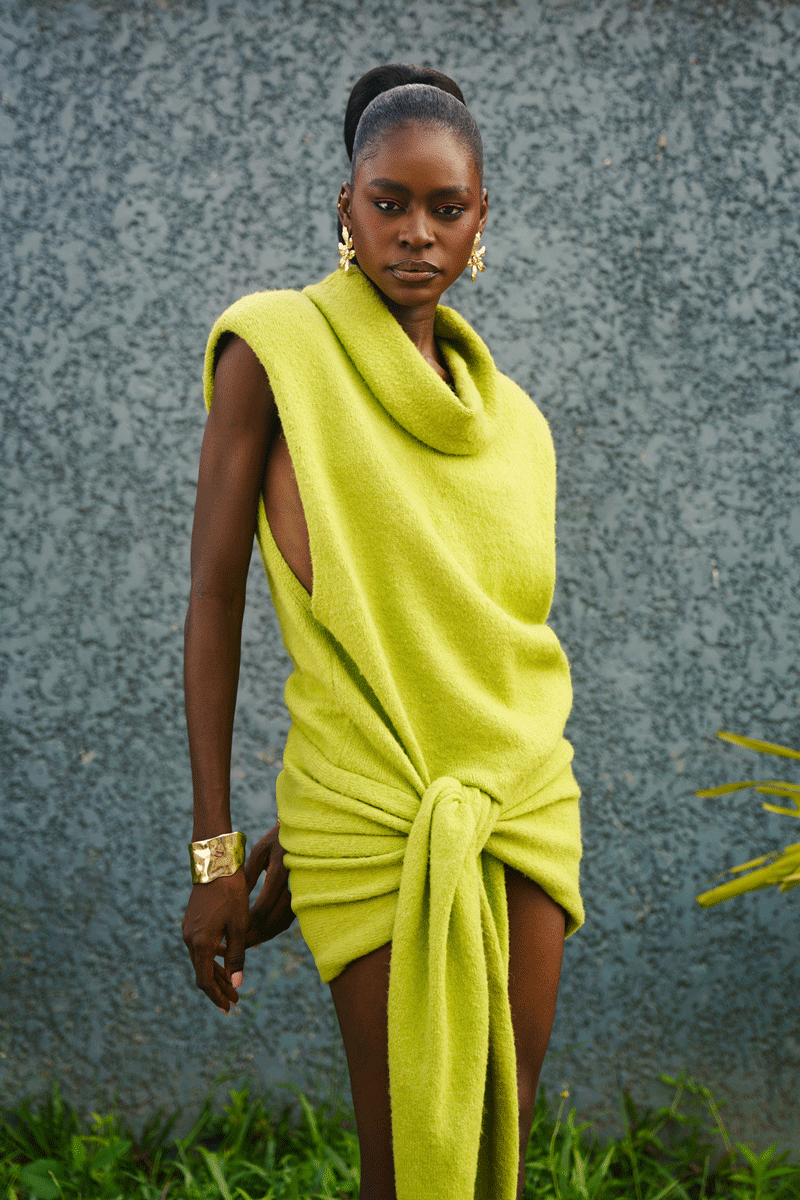 Woman wearing a bright green dress against a textured wall.