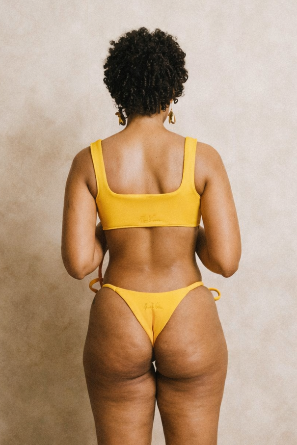 Person wearing a yellow bikini standing in a room with a decorative mirror and vase.