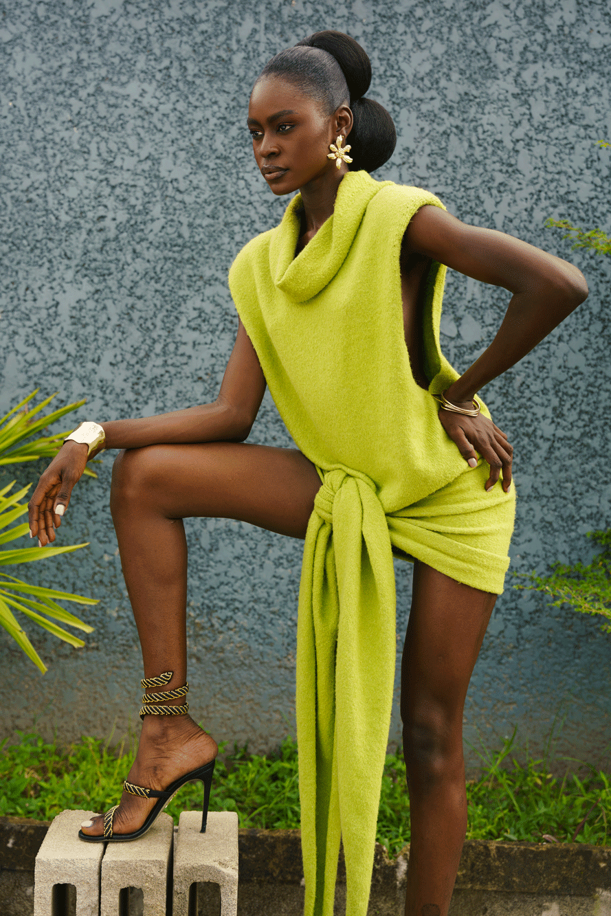 Woman in a bright green outfit posing outdoors with plants and a textured wall background